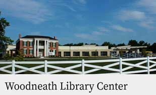 Woodneath American Colonial style building with columns, sitting on a hill with a fence in front of it